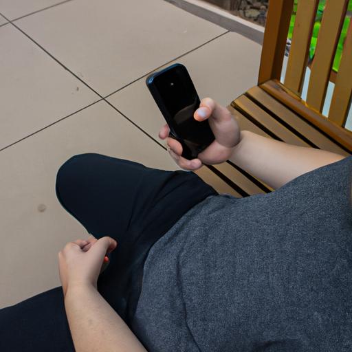 Một người nhìn chằm chằm vào màn hình điện thoại trong khi ngồi trên ghế đá.